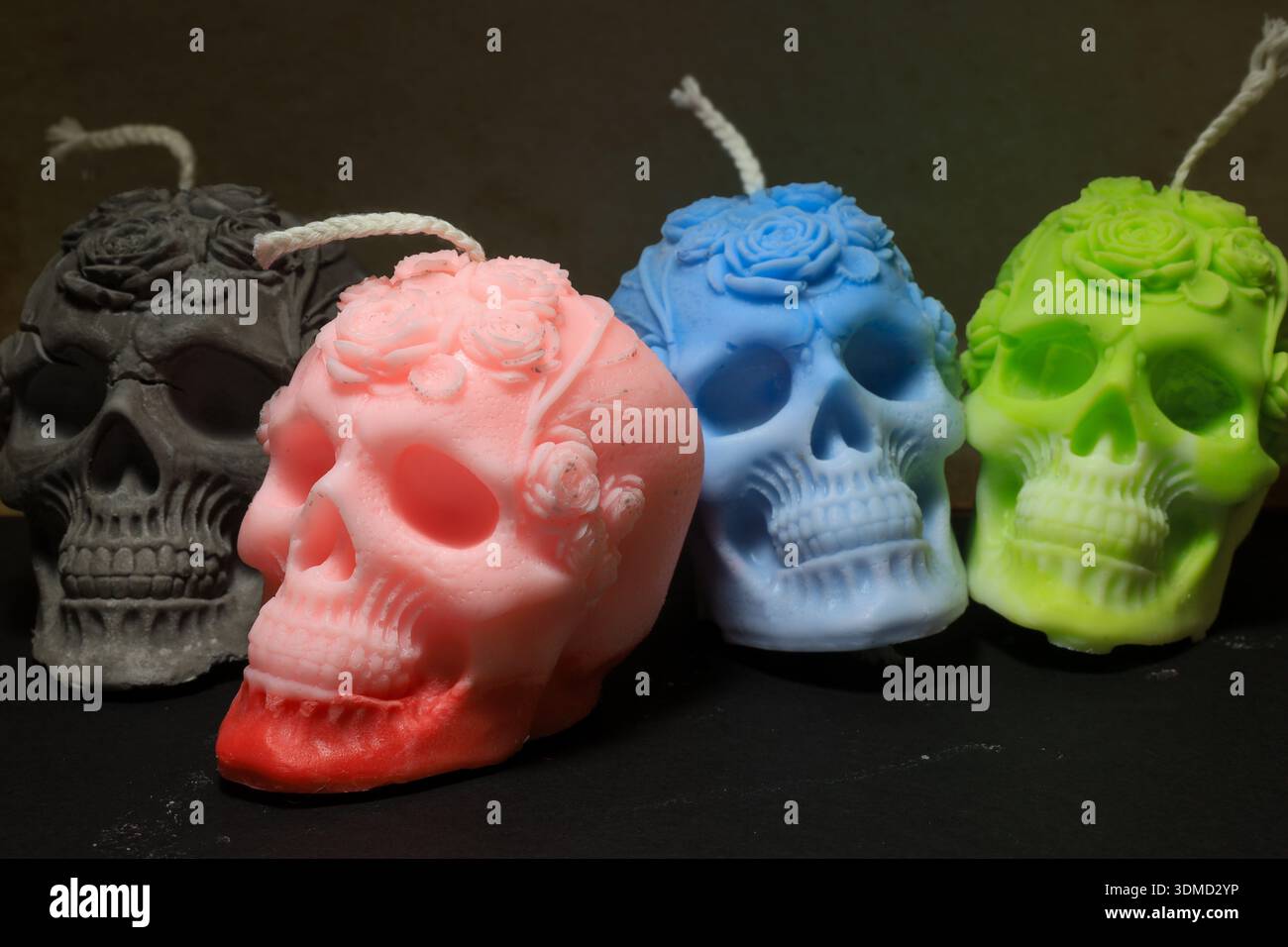 Four detailed skull-shaped candles in vibrant colors, each featuring floral crown motifs. Stock Photo