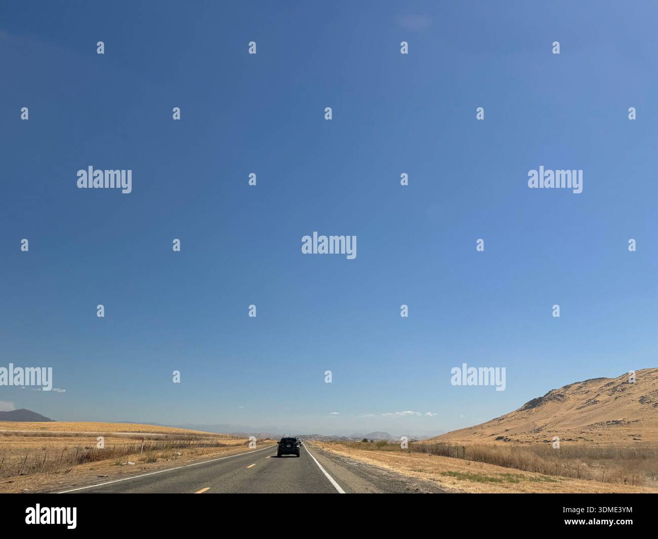 Cars driving along open highway through dry hills under clear blue sky in California, USA. - Smartphone Captured Stock Image
