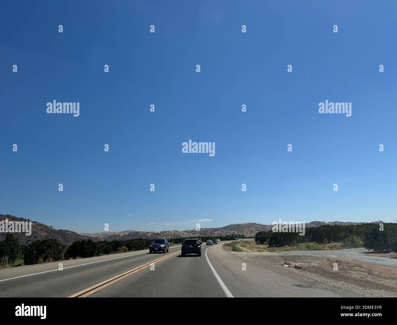 Cars driving along open highway through dry hills under clear blue sky in California, USA. - Smartphone Captured Stock Image