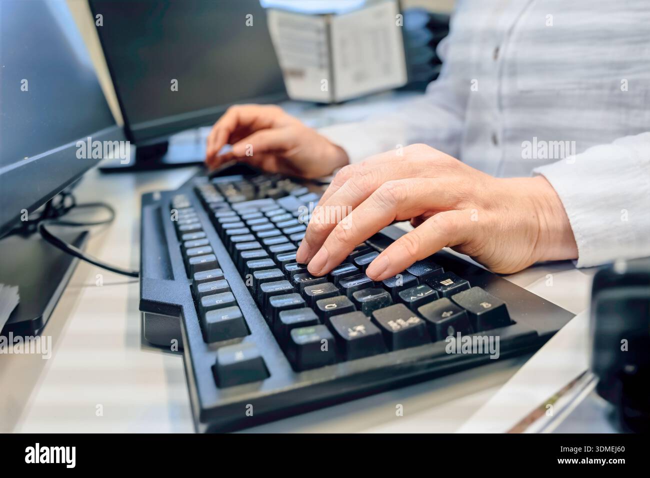 Skilled precision close view of woman hands typing on computer keyboard at office desk, white long sleeve , shallow depth workspace with monitor and d Stock Photo