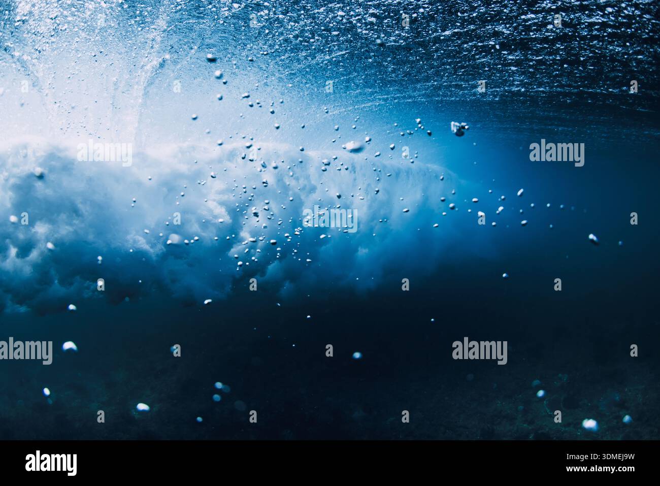 Underwater view of breaking ocean wave, blue water with sun light rays and bubbles Stock Photo