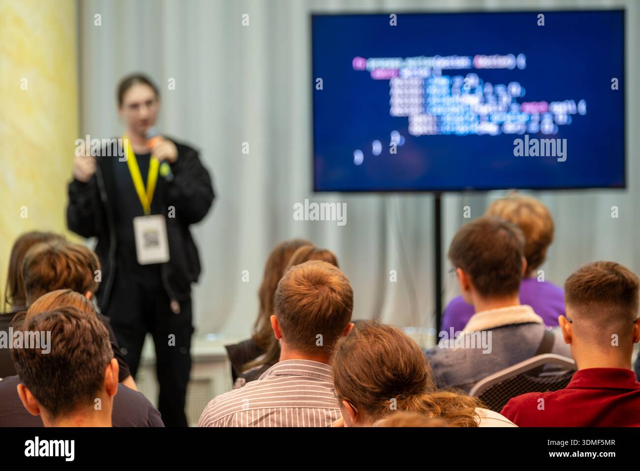 Audience listens to speaker during tech talk as code appears on screen. Stock Photo