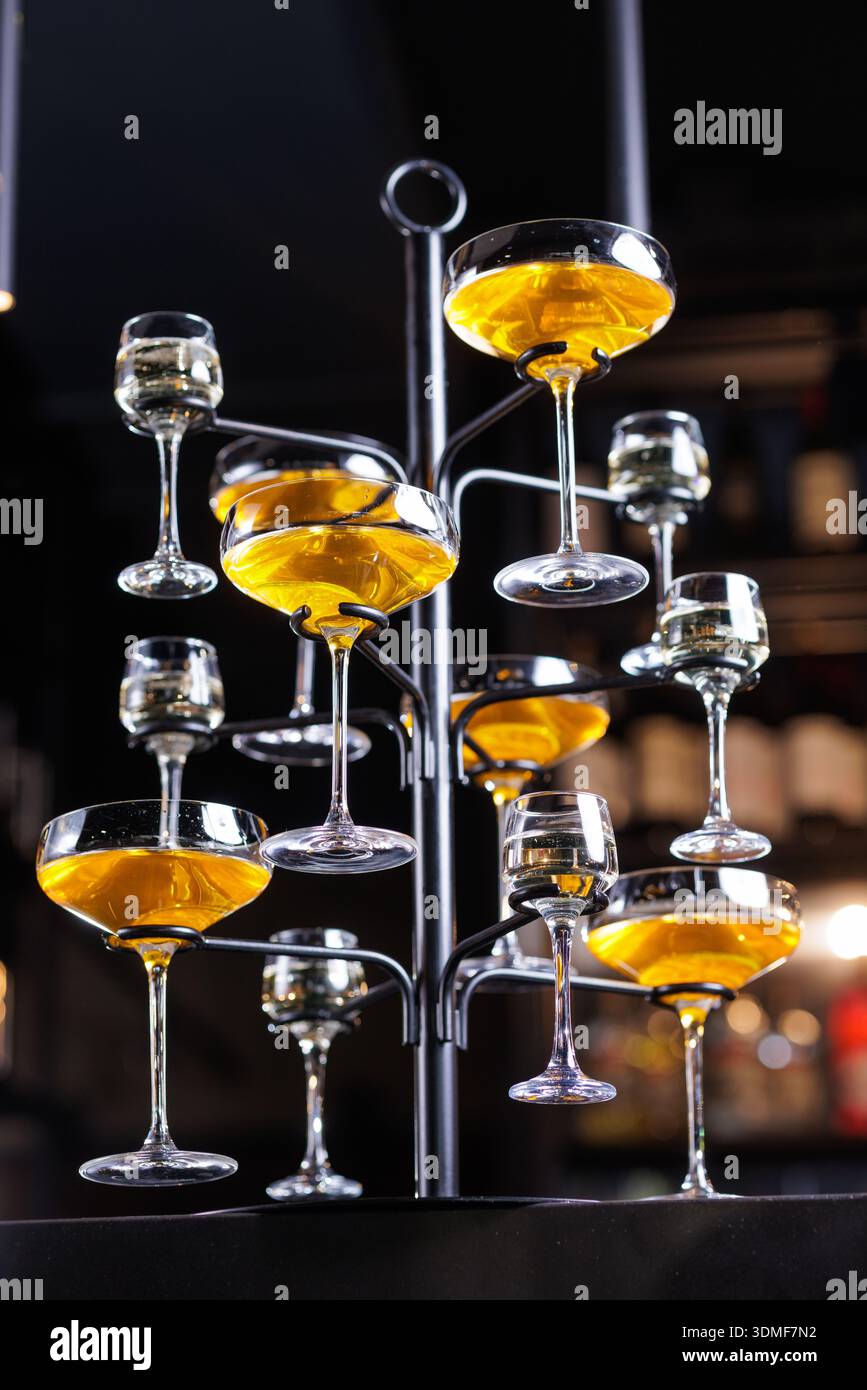 Multiple coupe glasses filled with cocktails arranged on display stand in bar. Ideal for hospitality, nightlife, and premium beverage marketing visual Stock Photo