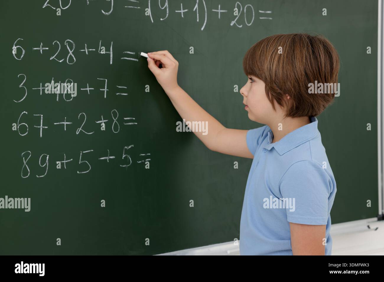Schoolboy doing math on chalkboard in classroom Stock Photo