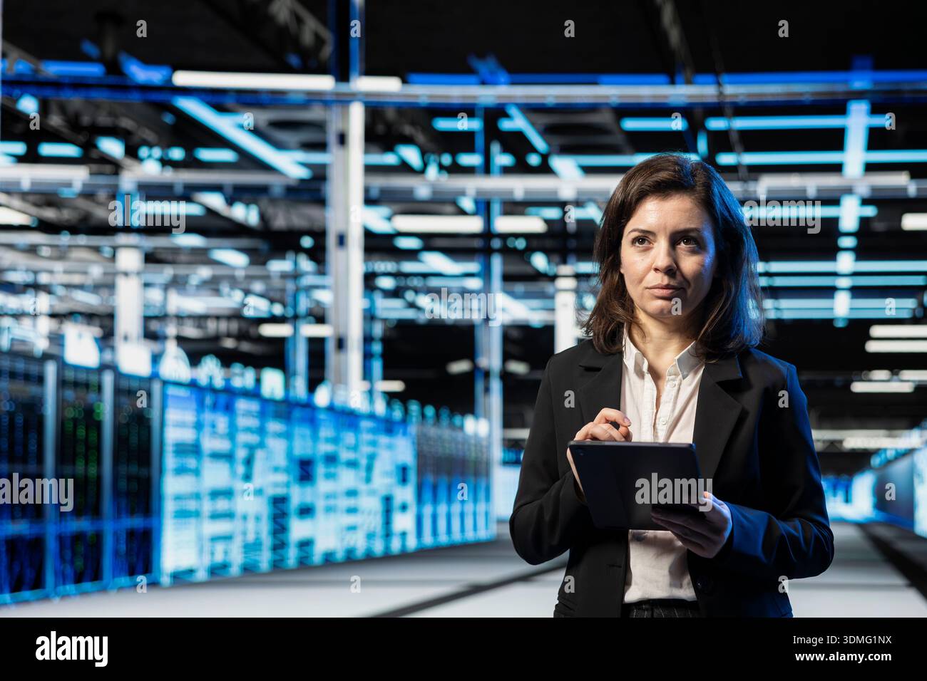 Data center technician using tablet to do checkup on cloud computing infrastructure, VFX compositing overlay. Server room employee walking between blue wireframe mainframes using device Stock Photo