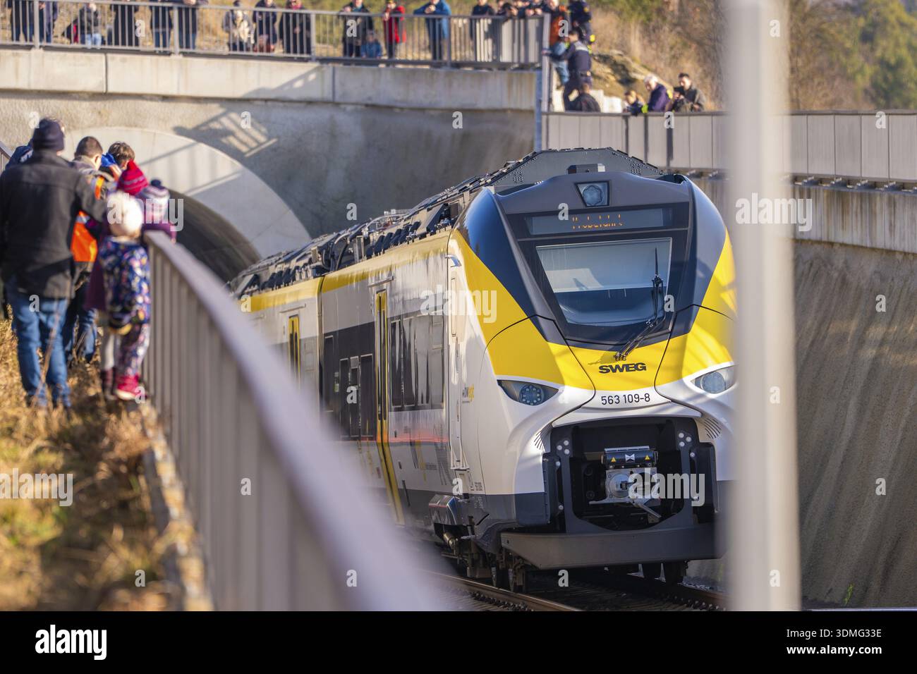 The yellow and white train passes a bridge. People are standing on the ...