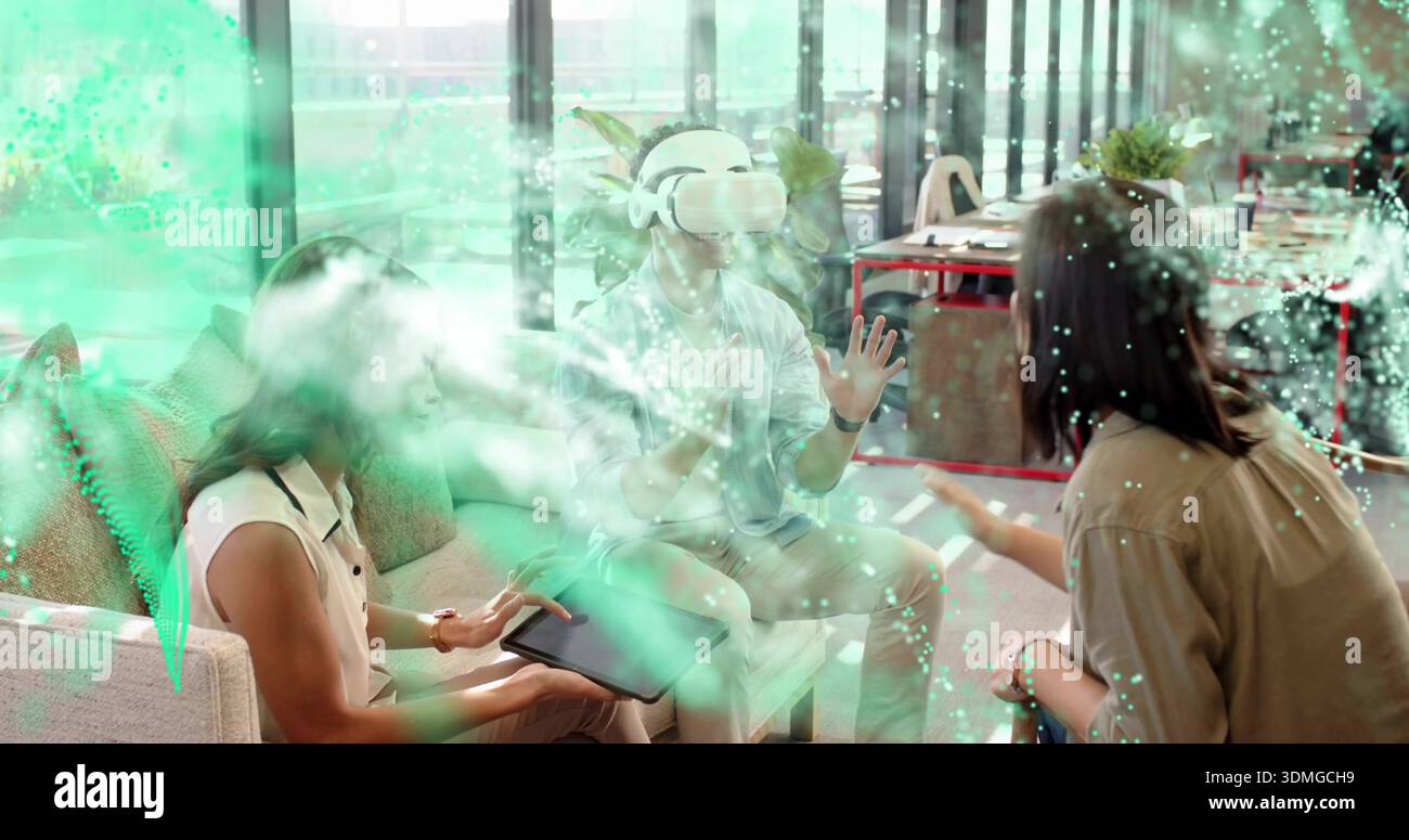 Showing team using VR headset and tablet in office lounge, displaying augmented interface Stock Photo