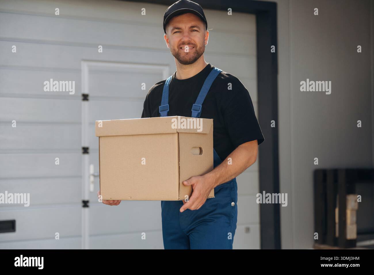 Mailing delivery service worker is in blue uniform, holding box. Stock Photo
