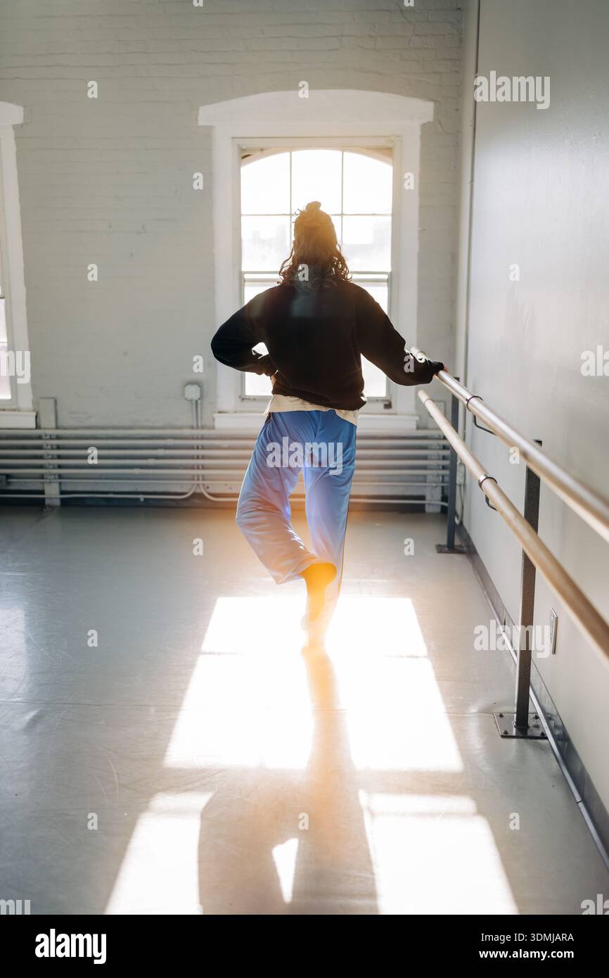 Dancer practicing ballet barre exercise in sunlit studio Stock Photo