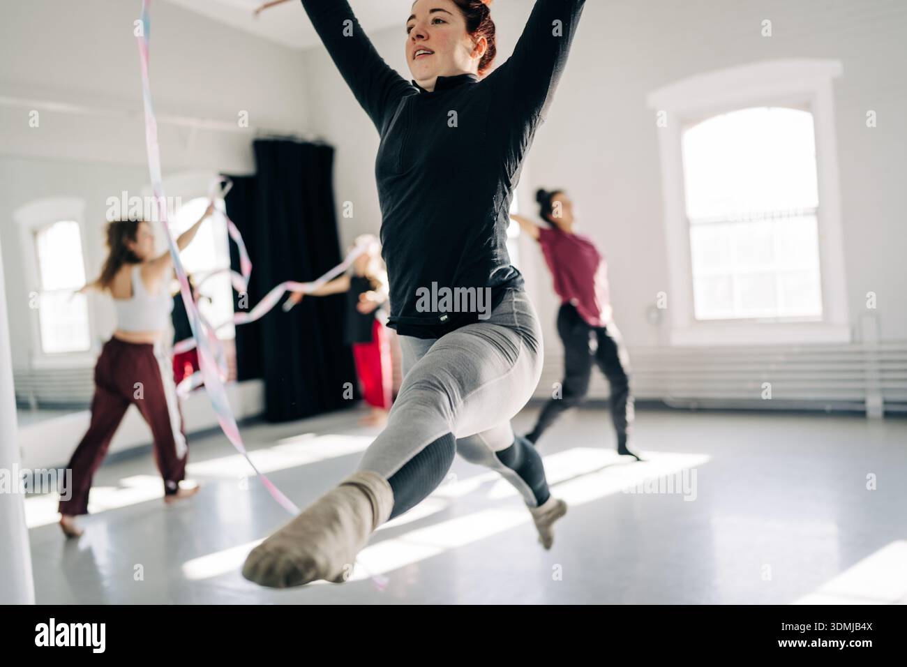 Gymnast performing rhythmic ribbon routine in bright studio Stock Photo