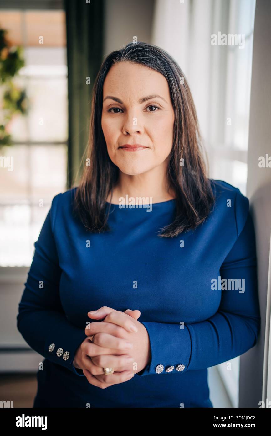 Professional woman standing with clasped hands by window Stock Photo