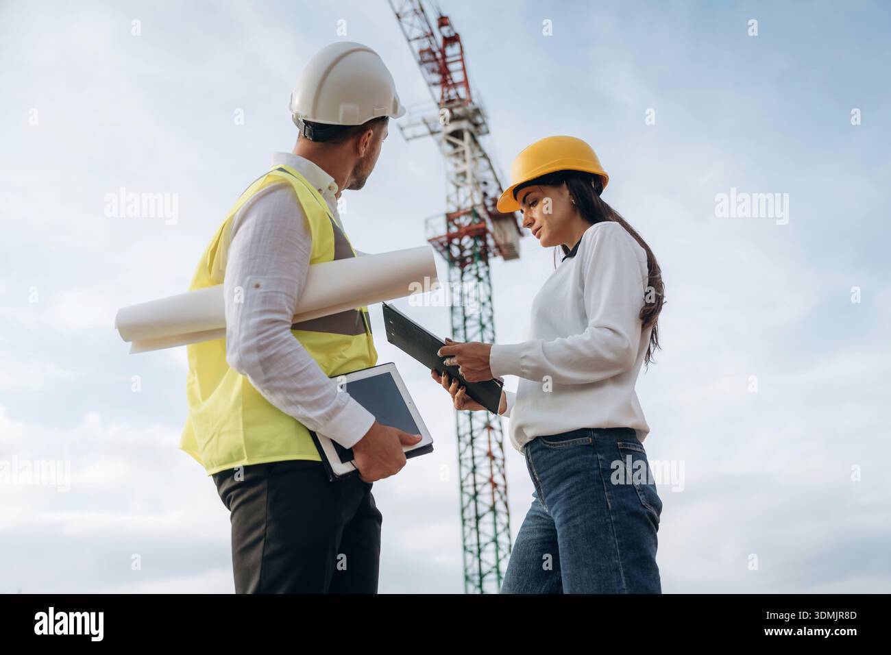 Man and woman, construction site workers are against crane, communication. Stock Photo