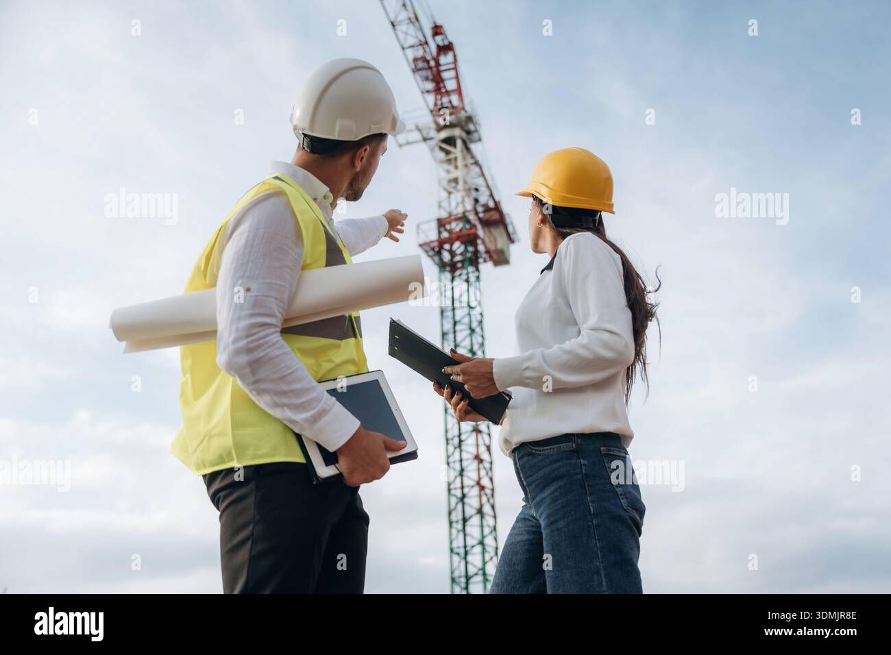Man and woman, construction site workers are against crane, communication. Stock Photo
