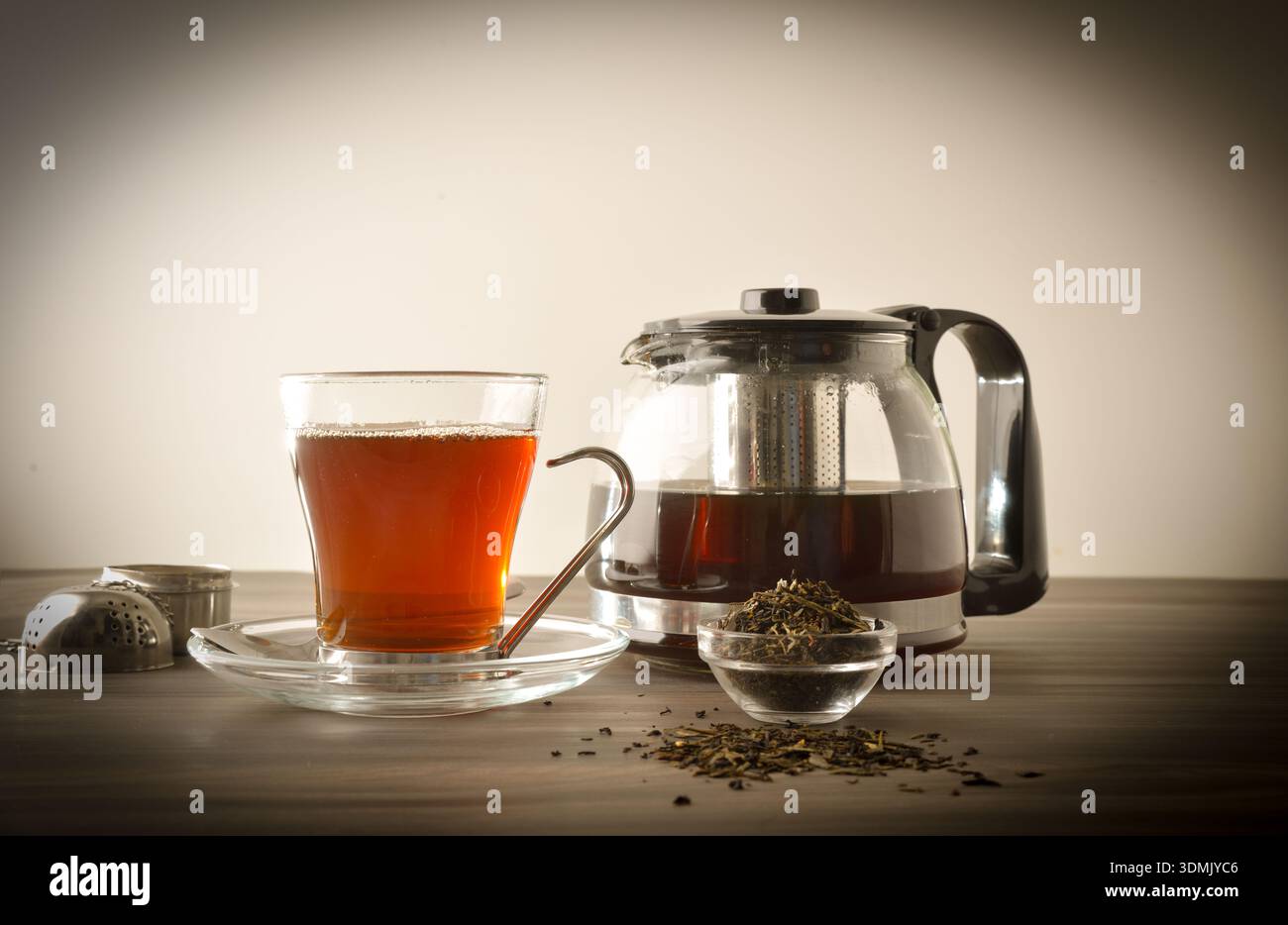Glass cup and teapot full of tea on a wooden bench with a bowl of dried tea leaves with white isolated background. Front view. Stock Photo