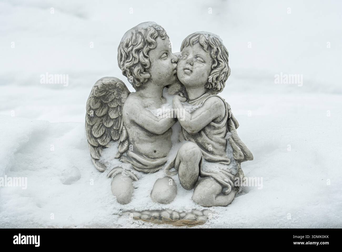 Two childlike angels kissing, sitting outdoors covered in fresh snow, symbolizing love, innocence, and serenity Stock Photo