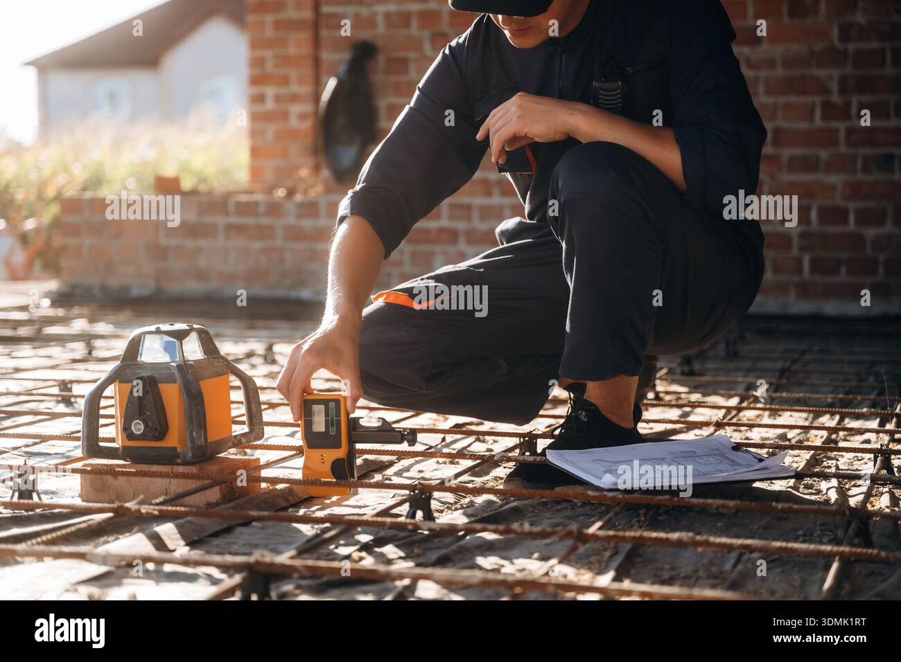 Sitting and using leveling tool. Builder is working on construction site, unfinished building. Stock Photo