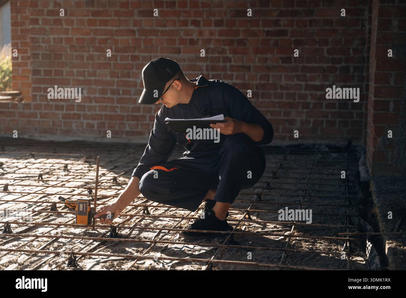 Sitting and using leveling tool. Builder is working on construction site, unfinished building. Stock Photo