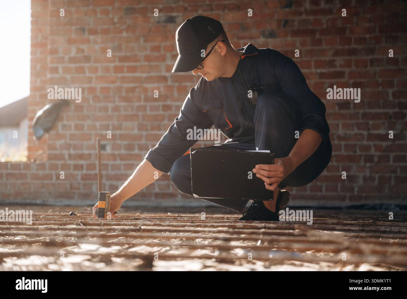 Sitting and using leveling tool. Builder is working on construction site, unfinished building. Stock Photo