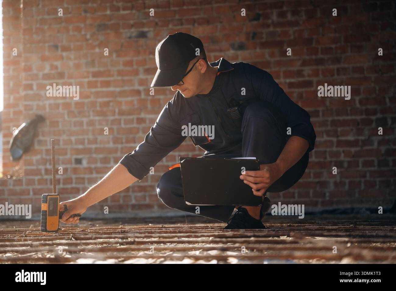Sitting and using leveling tool. Builder is working on construction site, unfinished building. Stock Photo