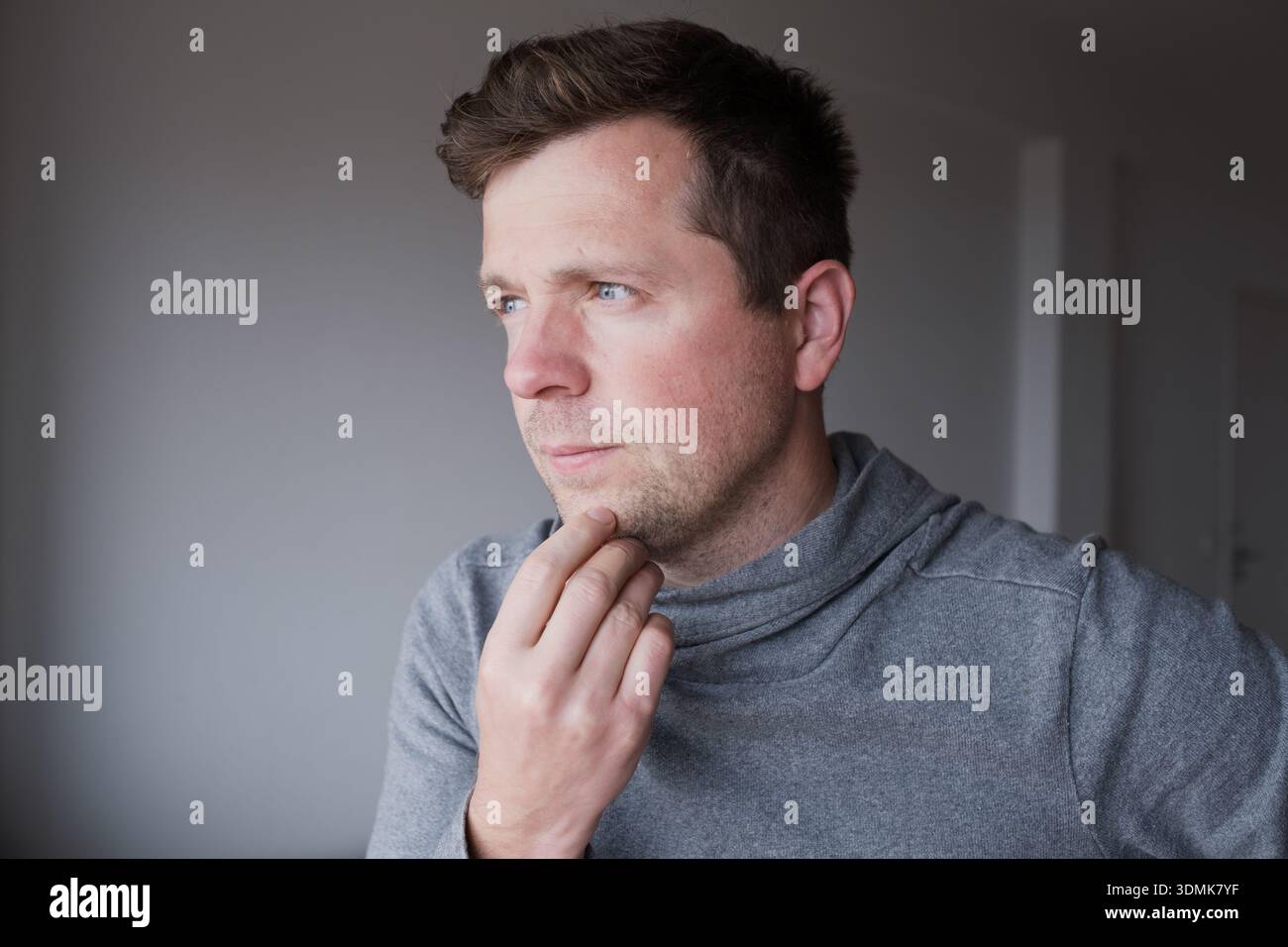 Pensive young man standing at home thinking about problems and making decisions Stock Photo