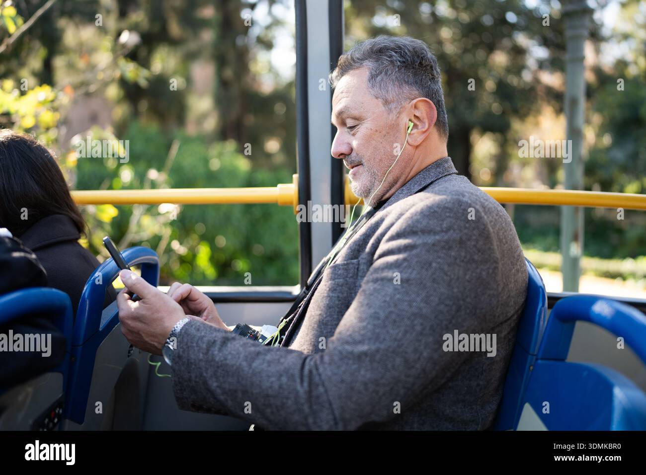 Mature man commuting on bus using smartphone and earbuds Stock Photo