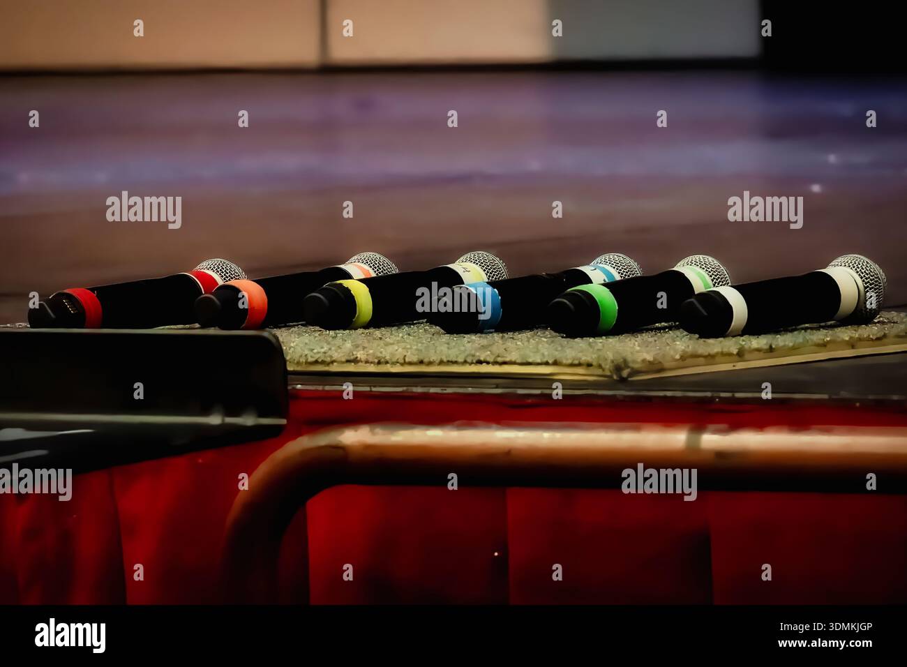 Row of handheld microphones with colorful identification bands resting on stage before a live performance, illuminated under stage lighting. Stock Photo