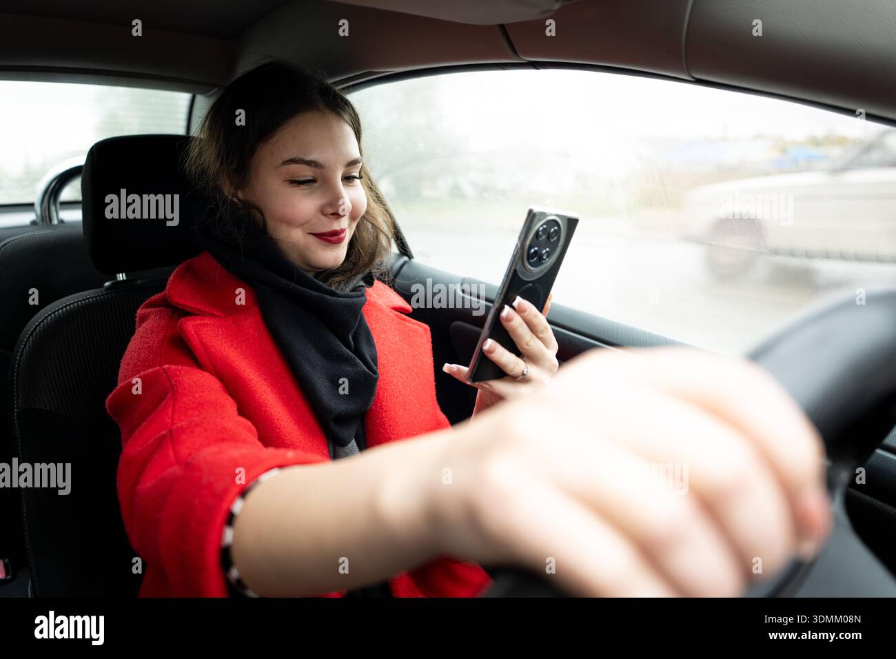 caucasian woman sits in a car, distracted and looking at a smartphone message in her hands, illustrating the danger of texting while driving. Stock Photo
