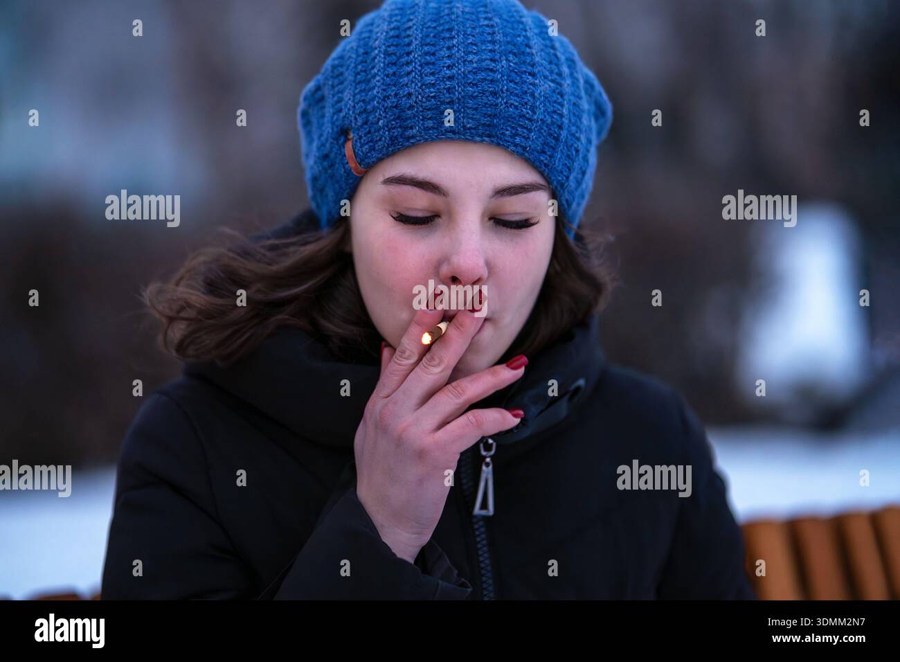 she smokes cigarettes Girl smokes a cigarette. Woman smokes cigarettes. close-up of a young woman  smoking on a cold winter evening. Tobacco smoke Stock Photo