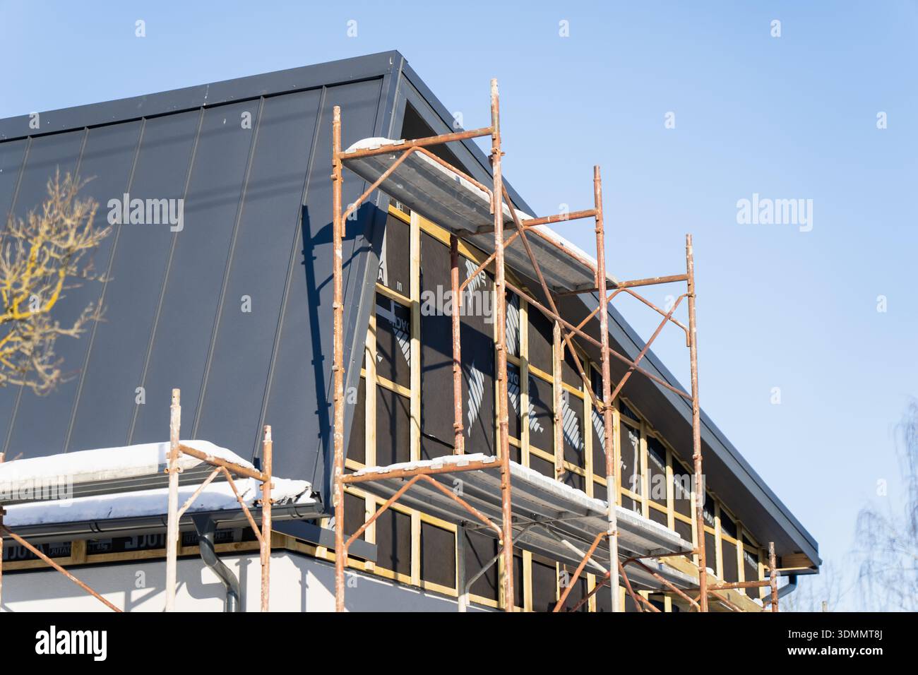 Modern house renovation with rusty scaffolding on dark metal roof gable ...