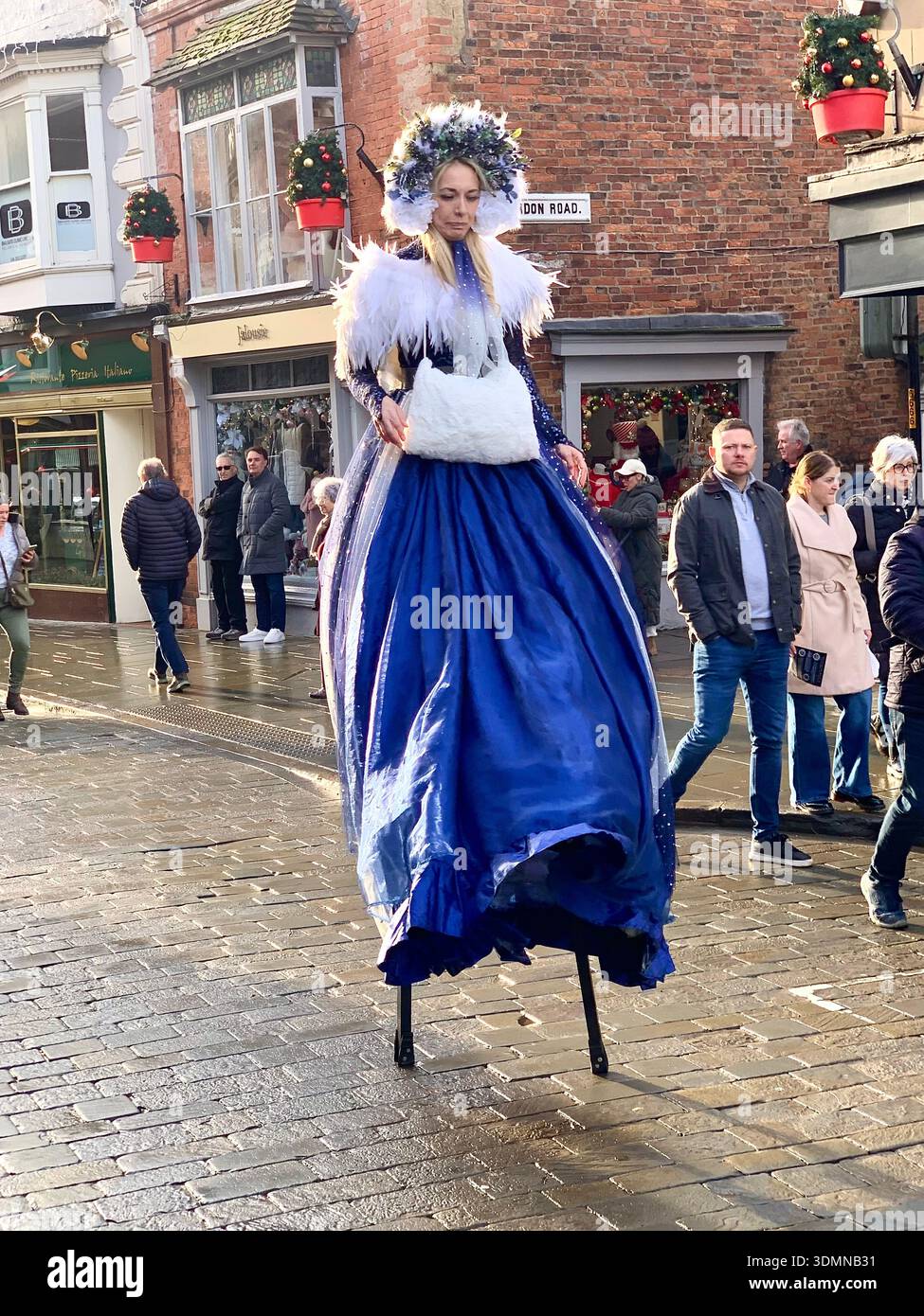 Stilt walker in an ornate blue costume entertaining shoppers on a Lincoln high street during a festive event  in Lincoln high street England lady - Smartphone Captured Stock Image