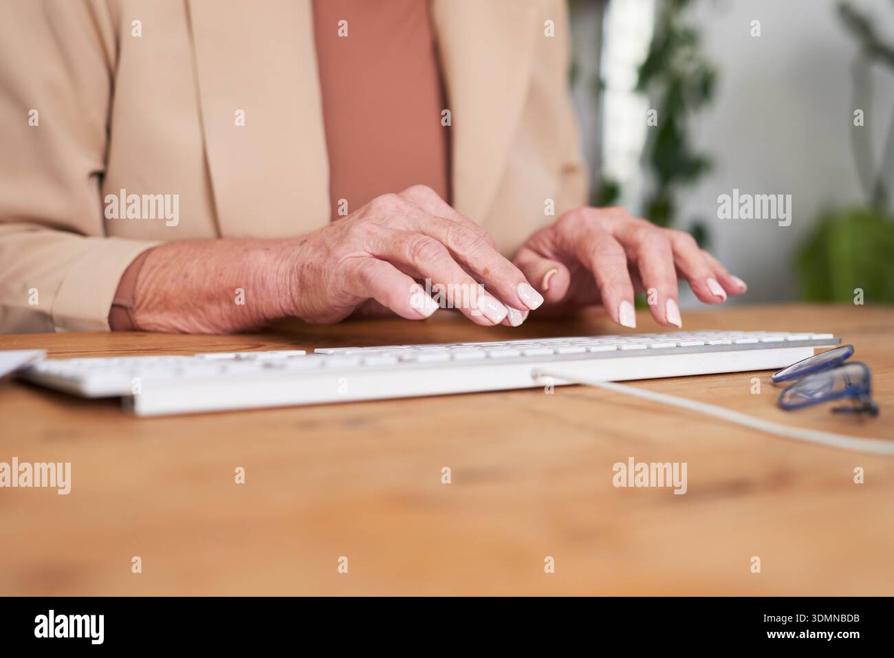 Senior Woman Typing On Keyboard At Desk With Glasses In Modern Home Office Stock Photo