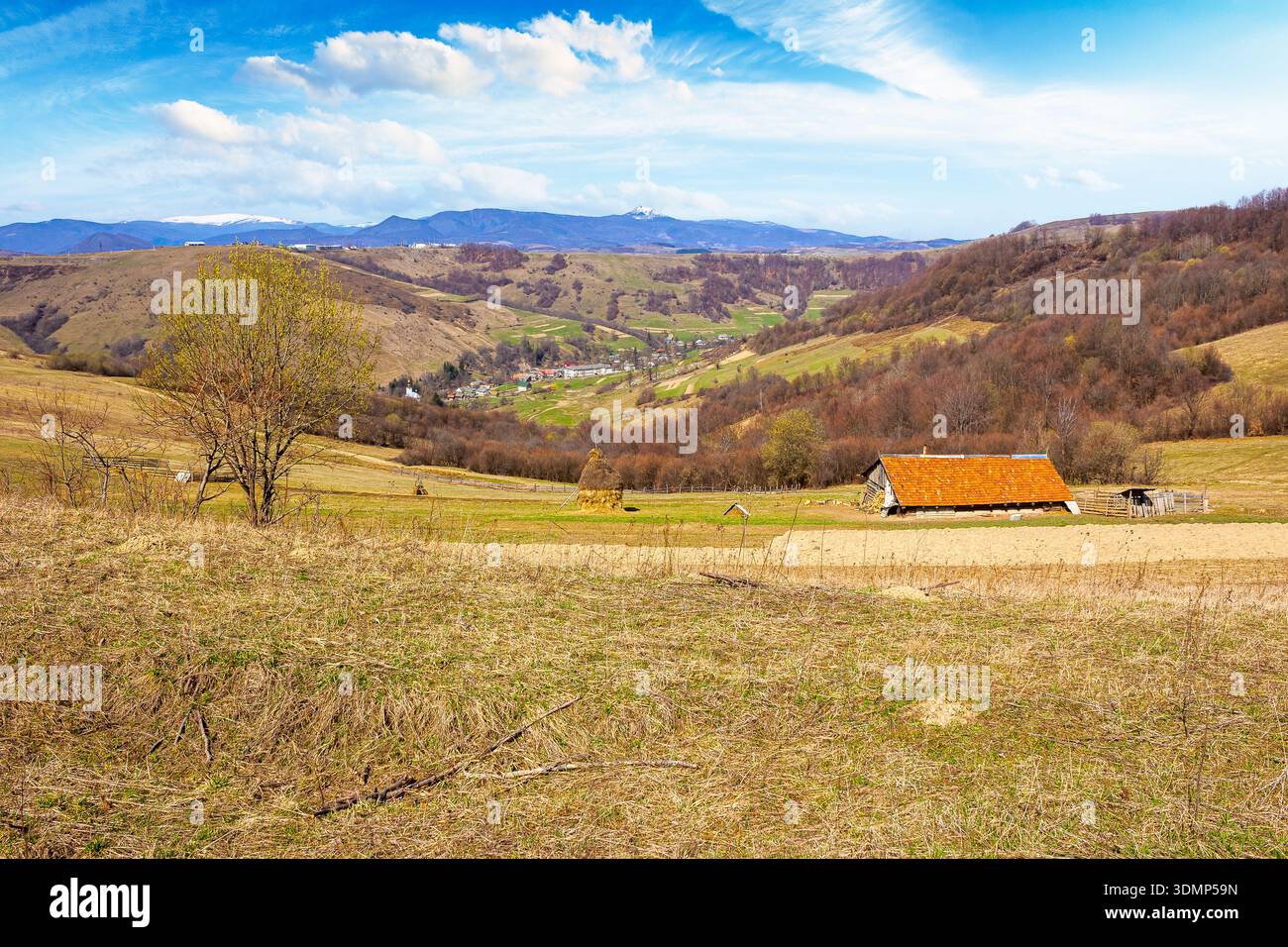 rural landscape with village in valley. outdoor adventures in countryside with rolling hills and snowy mountains in early spring. green environment su Stock Photo