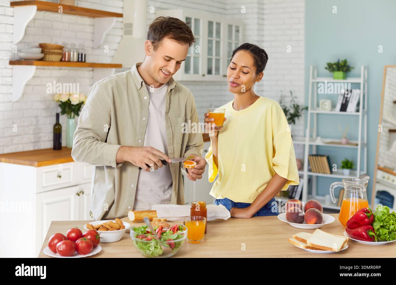 Couple preparing toast with jam and drinking juice together in bright kitchen Stock Photo