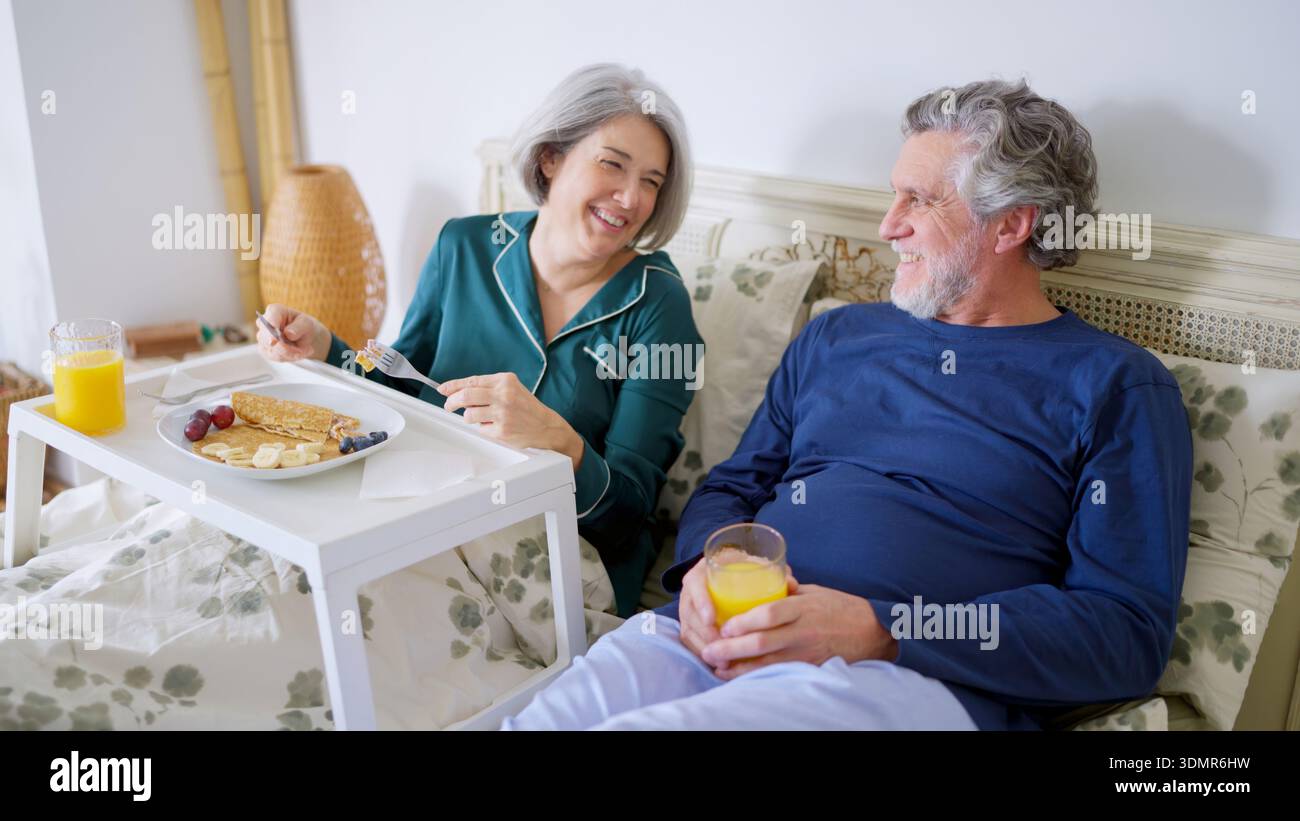 Senior couple sharing a joyful breakfast in bed Stock Photo