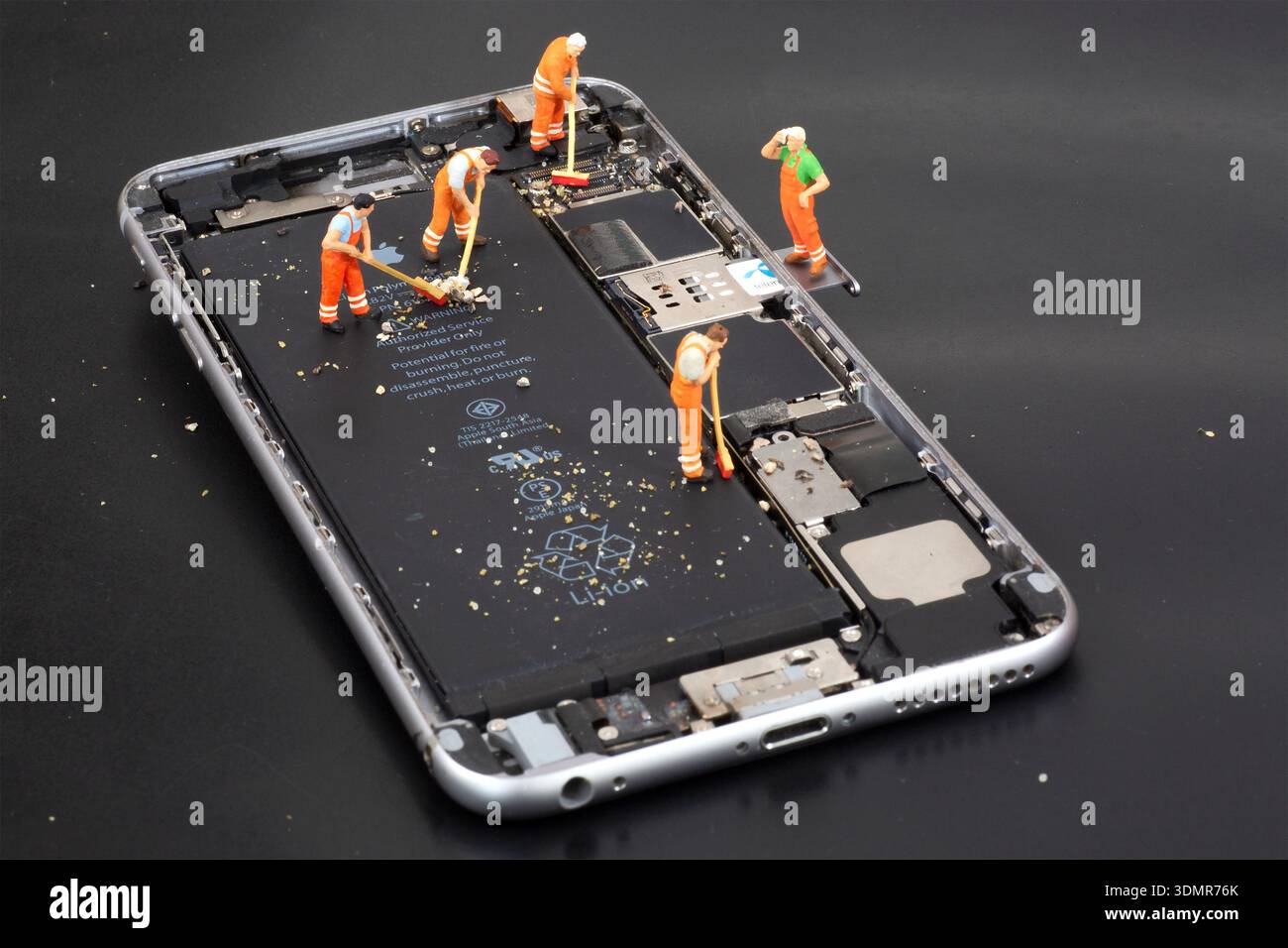 Miniature workers staged inside a smartphone interior for editorial illustration. Stock Photo