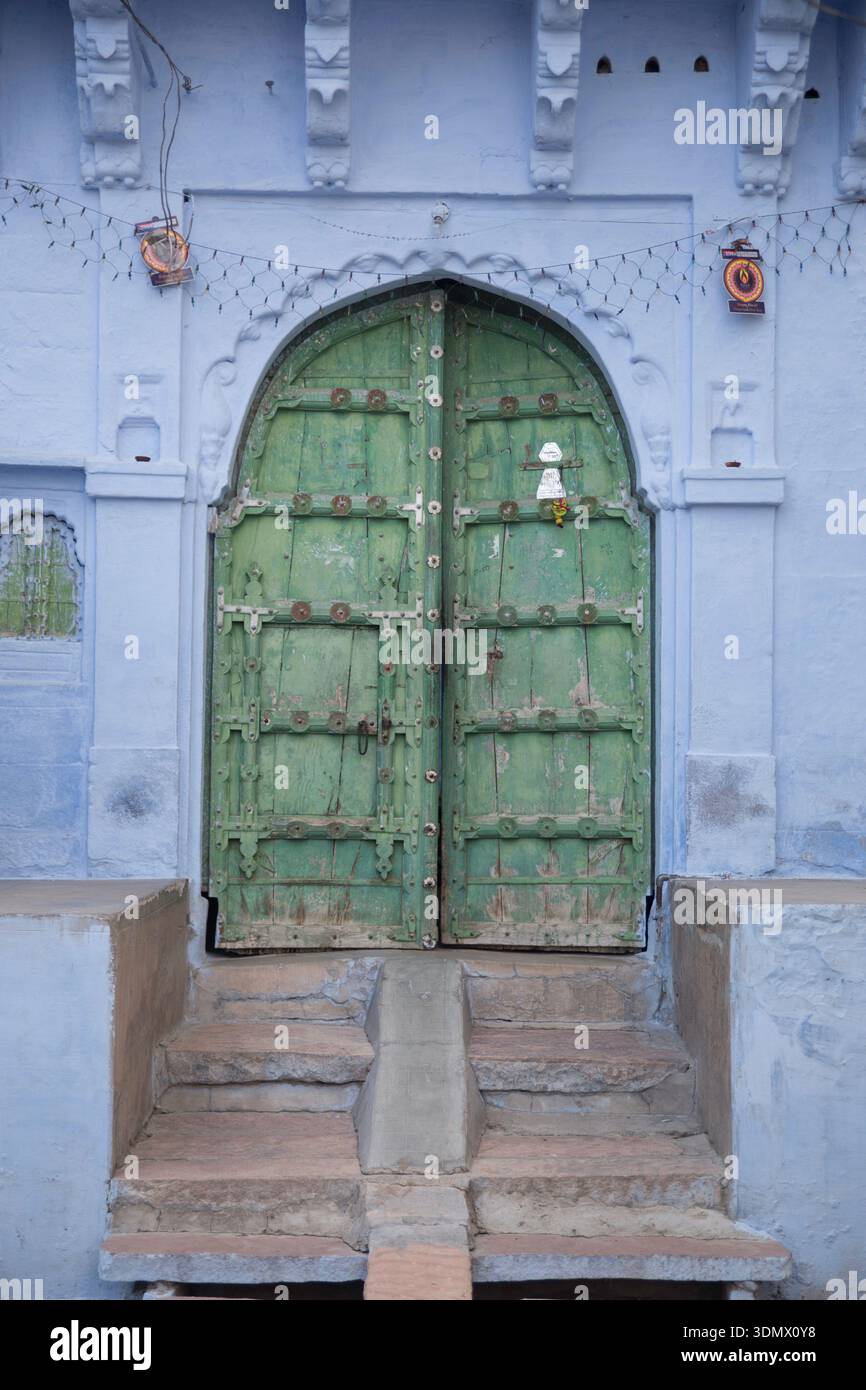 A weathered green door set against a blue wall in a traditional setting. Stock Photo
