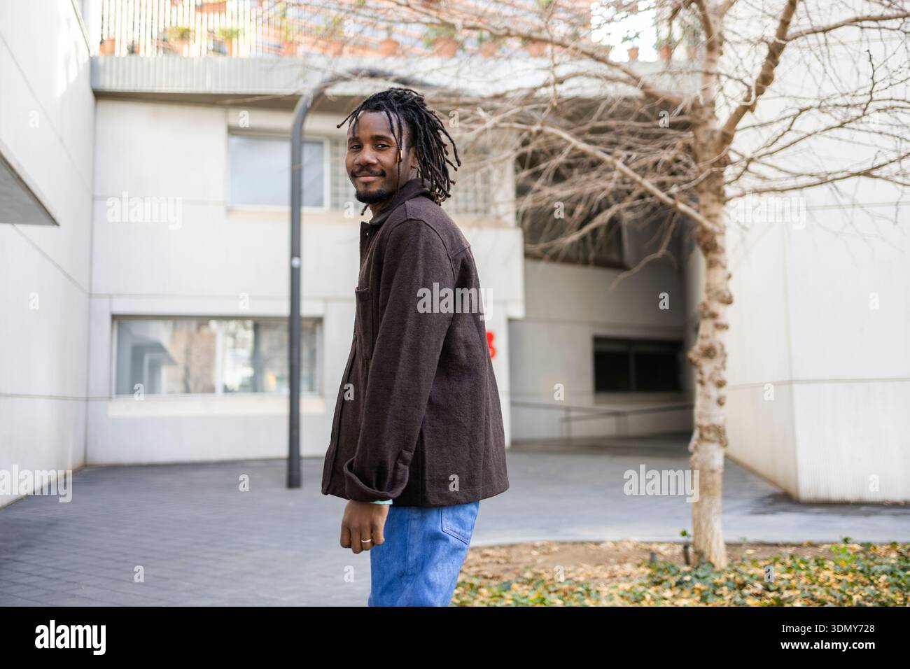 African American businessman with dreadlocks stands confidently in an urban setting, wearing a dark jacket and blue jeans. The scene exudes profession Stock Photo