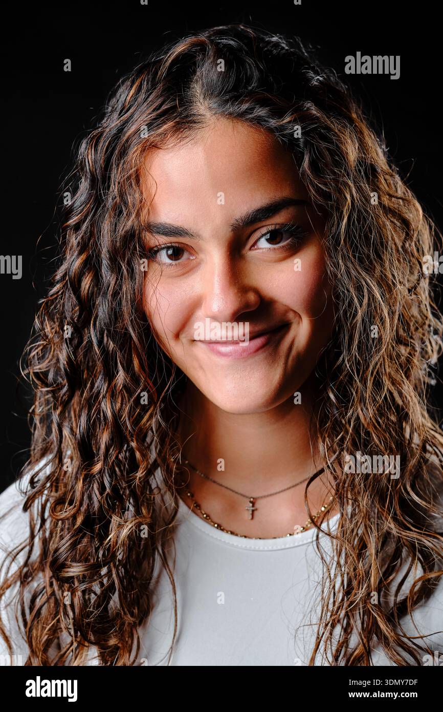 Smiling young woman with curly brown hair against a black background Stock Photo