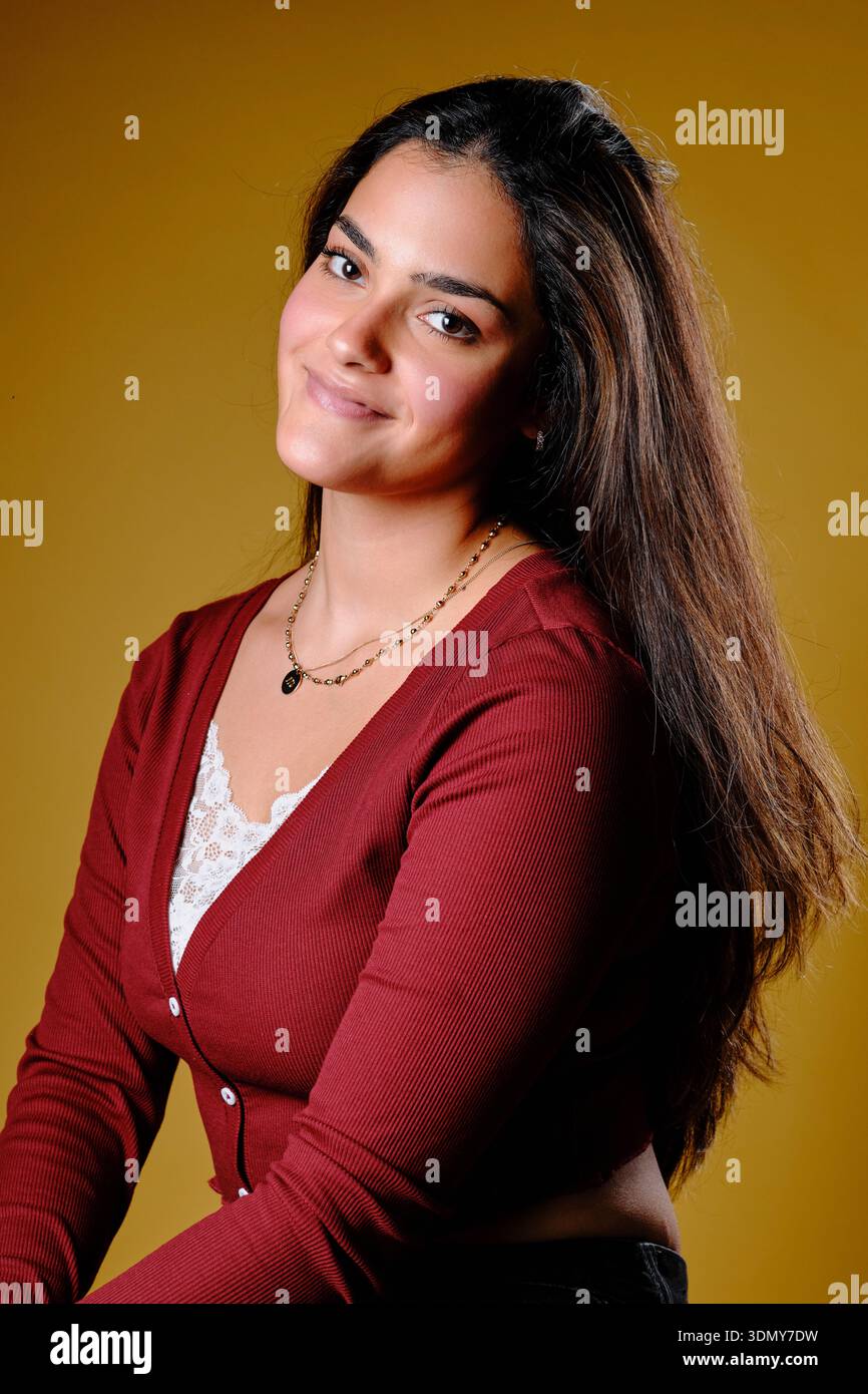 Young woman looking at camera, smiling, confidence, and youth with a plain gold background Stock Photo