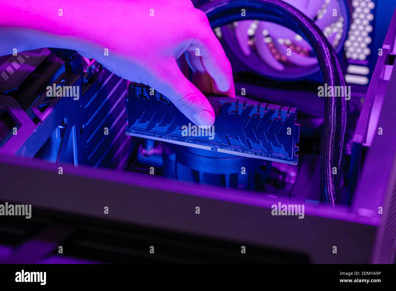 Installing RAM memory module into motherboard inside gaming computer, rgb lighting highlighting hardware upgrade, system assembly, performance computi Stock Photo