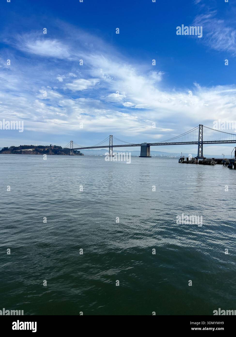 Scenic vertical view of the San Francisco–Oakland Bay Bridge and calm waterfront from a wooden pier in San Francisco, California. Peaceful coastal cit - Smartphone Captured Stock Image