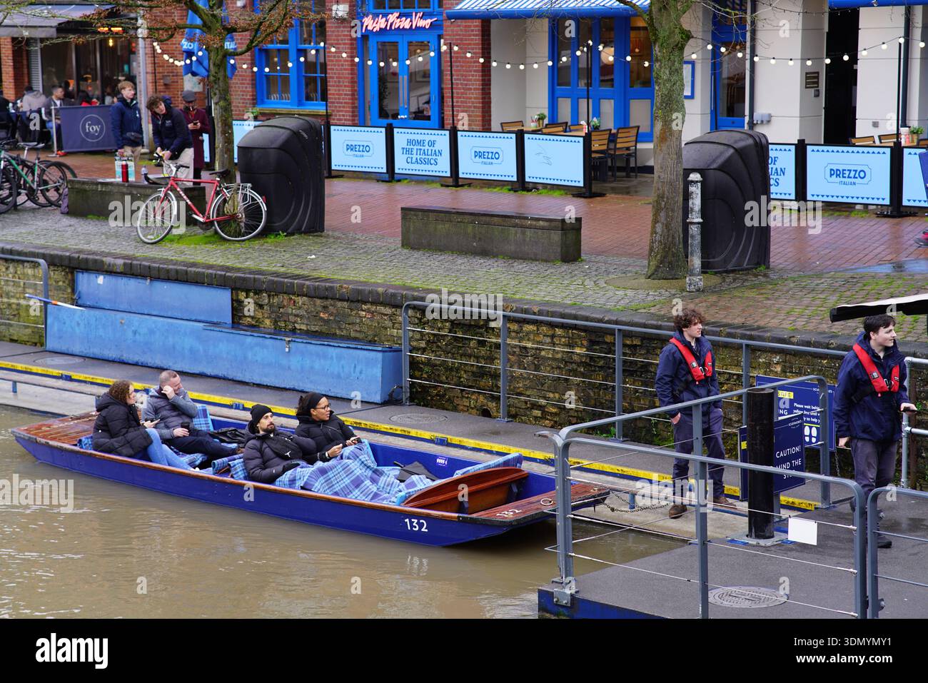 Punter guiding a blue punt with passengers under blankets on the River Cam at Cambridge Quayside in winter. Cambridge,England Stock Photo