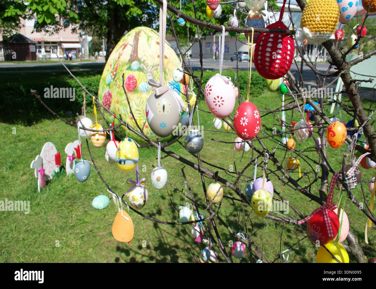 Festive Easter decorations with colorful handmade easter eggs hanging on tree branches in a city park. Handcrafted, painted, crocheted, and pattern. Stock Photo