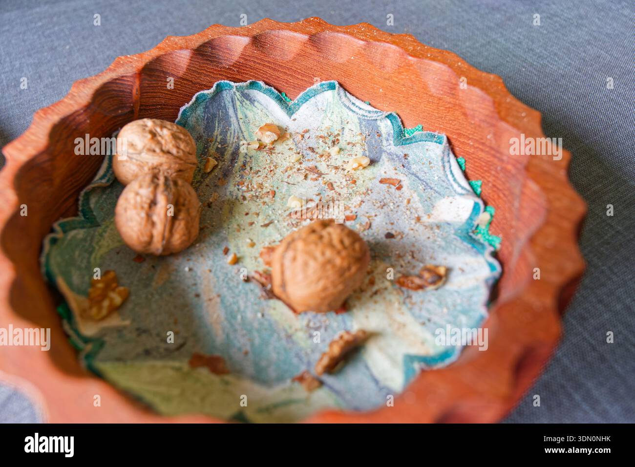 A carved wooden plate holds an embroidered napkin and three walnuts, arranged neatly on a table to create a simple rustic still life with natural text Stock Photo
