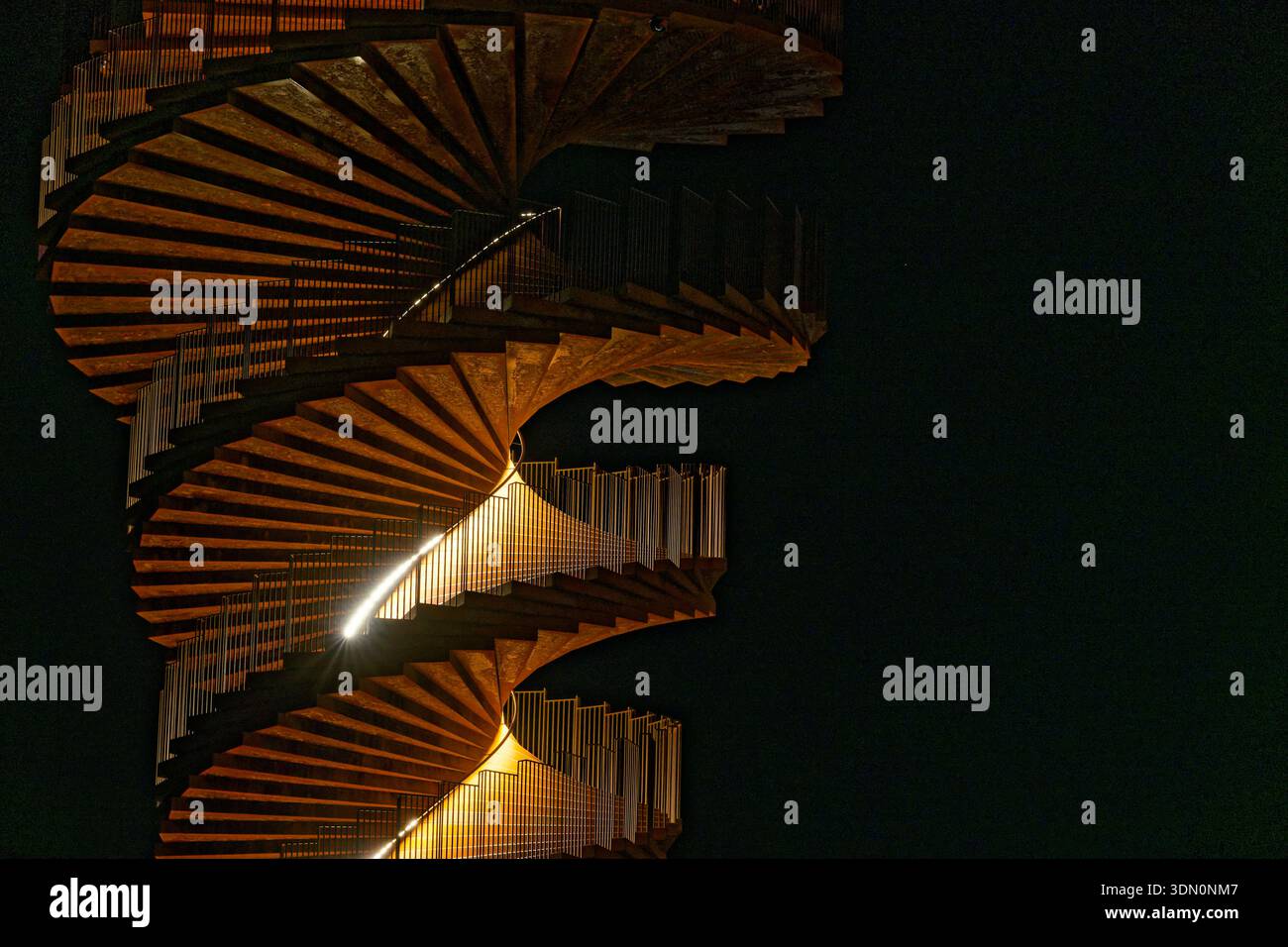 A spiral staircase climbs upward and widens as it rises, silhouetted against a dark sky. The unusual geometry creates a striking architectural shape a Stock Photo