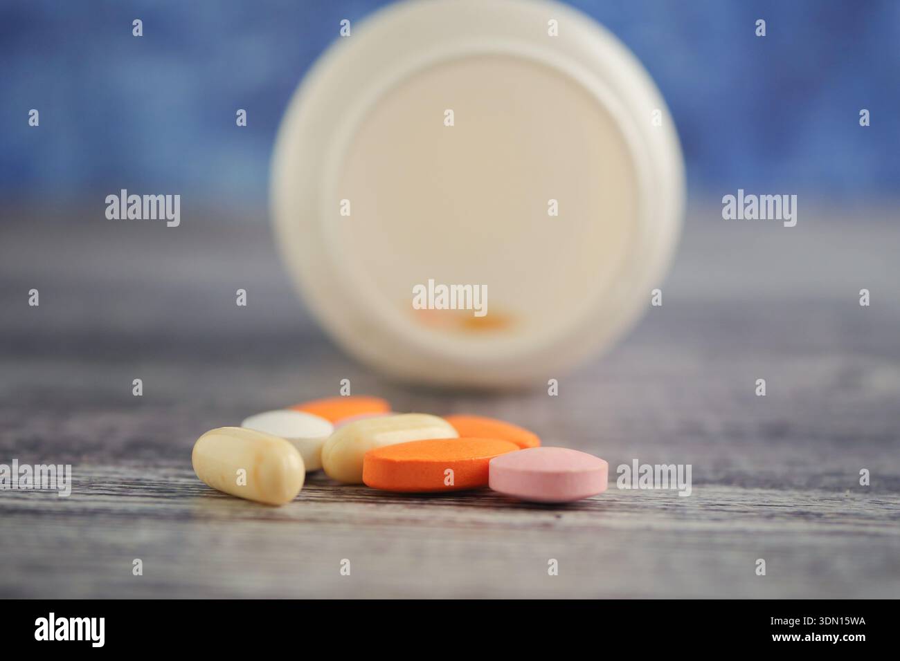 Various pills scattered near an open container on a surface Stock Photo