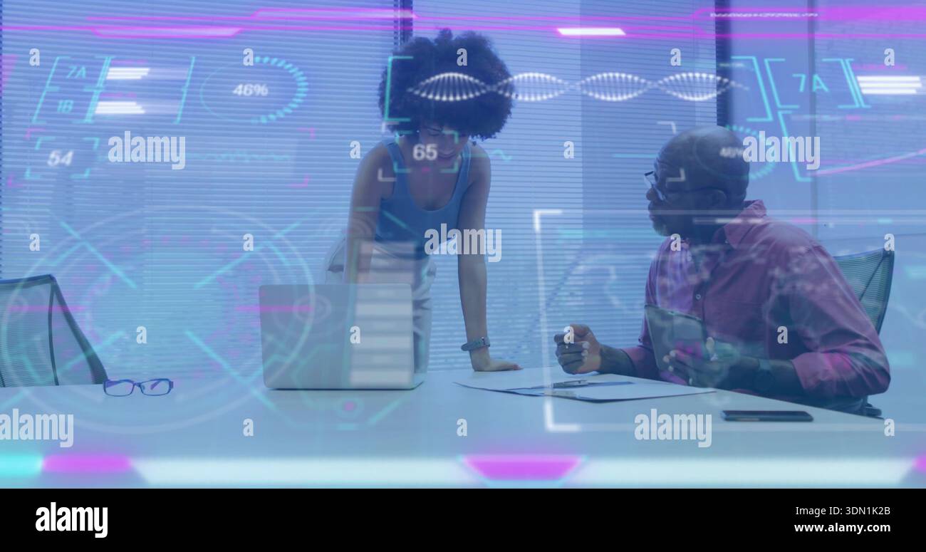 Analyzing, woman in blue top leaning over laptop and man holding papers in boardroom with holograms Stock Photo