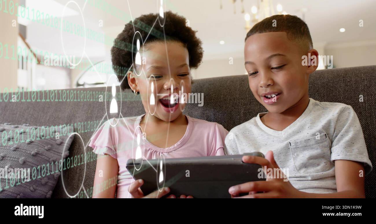 Sitting two children wearing gray tee and pink top, holding tablet in living room with overlays Stock Photo