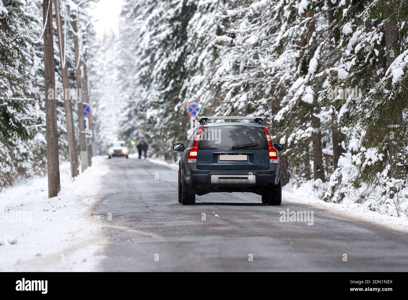 Car driving on frosty countryside road through spruce forest covered in snow on cold winter day. Stock Photo