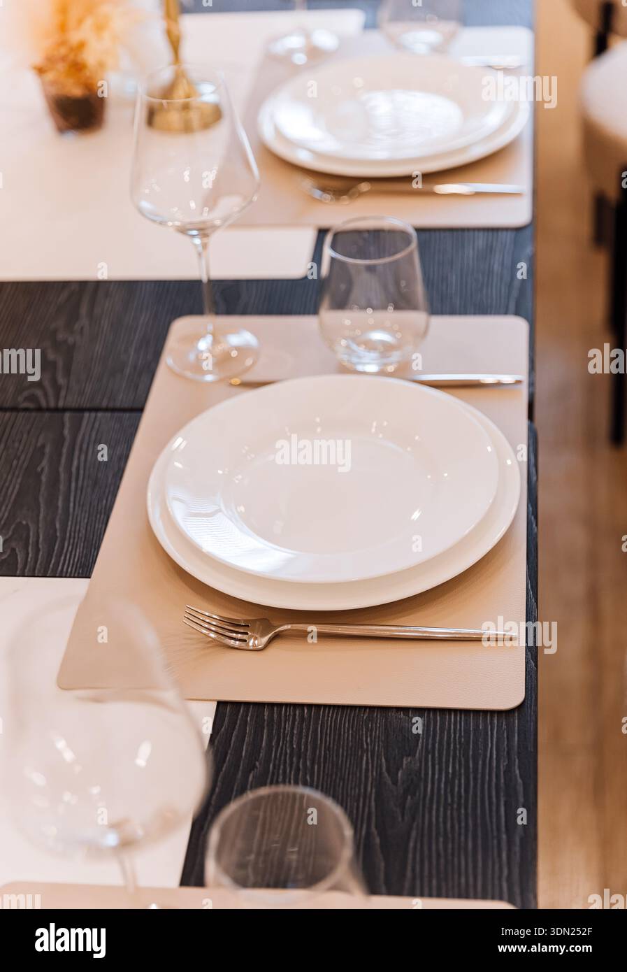 Minimal restaurant place setting with white plate, glassware, beige placemat Stock Photo
